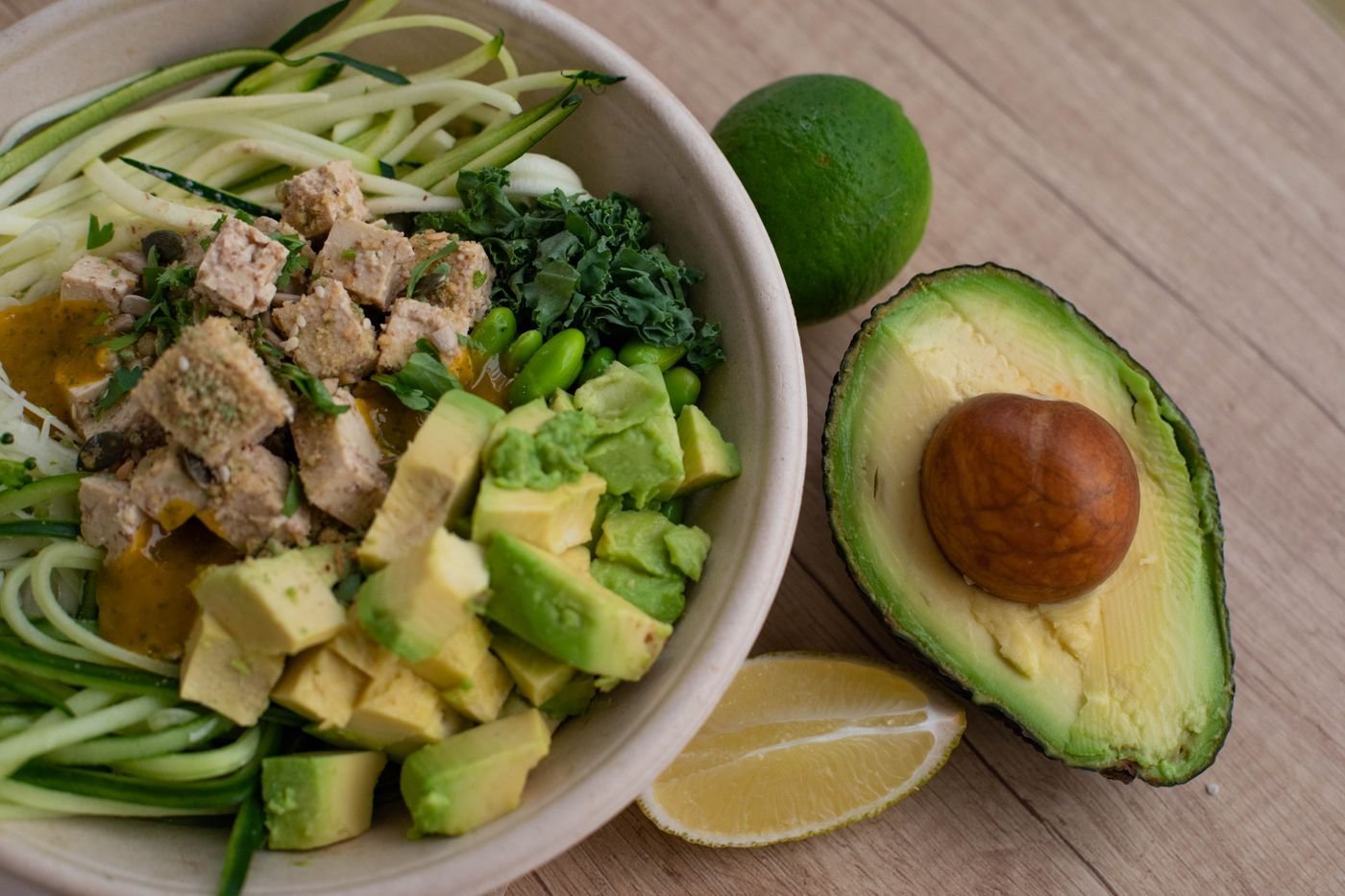 Bowl of zucchini noodles, avocado cubes, walnut crumble and kale with lime and avocado half