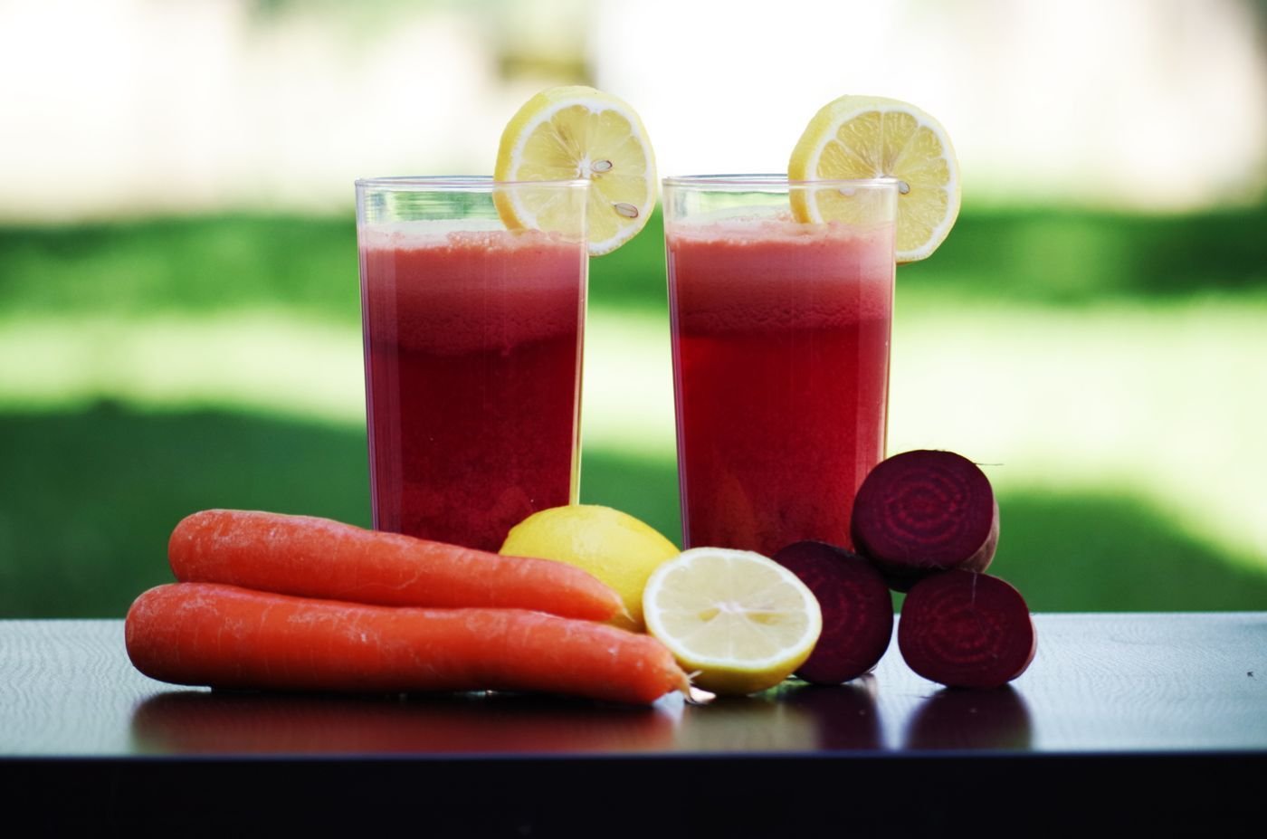 Two glasses of beet carrot juice with lemon slices, carrots and beets