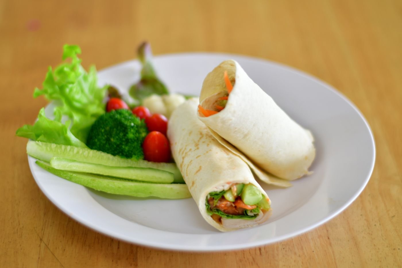 Wrap halves with cucumber sticks, broccoli and cherry tomatoes on a white plate