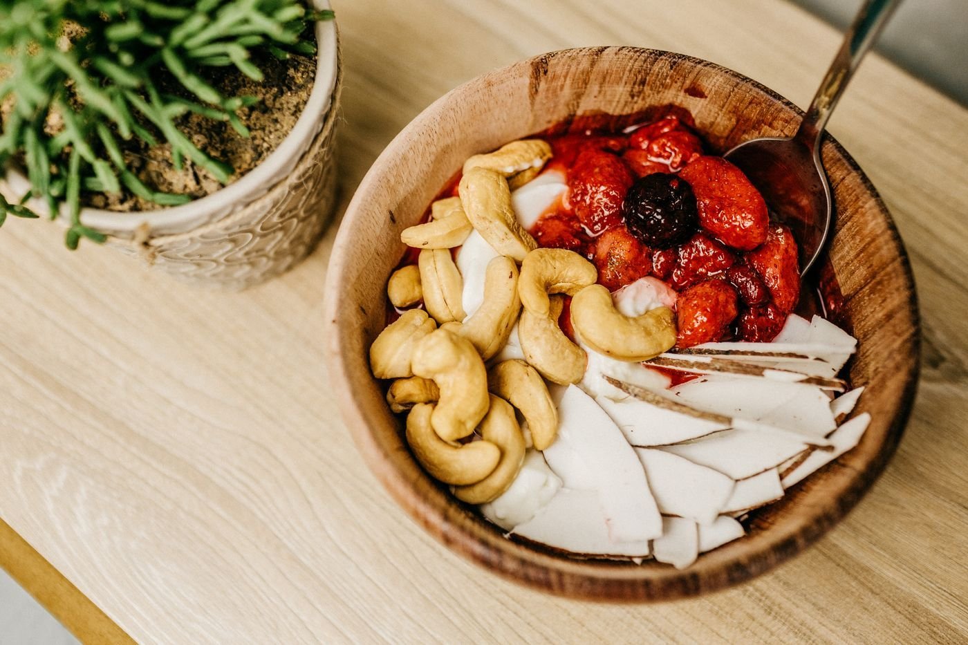 Wooden bowl of cashews, strawberries and coconut chips next to a plant