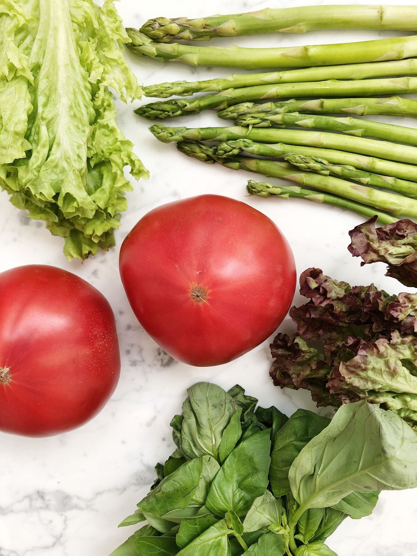 Heirloom tomatoes, asparagus, lettuce and basil on white marble
