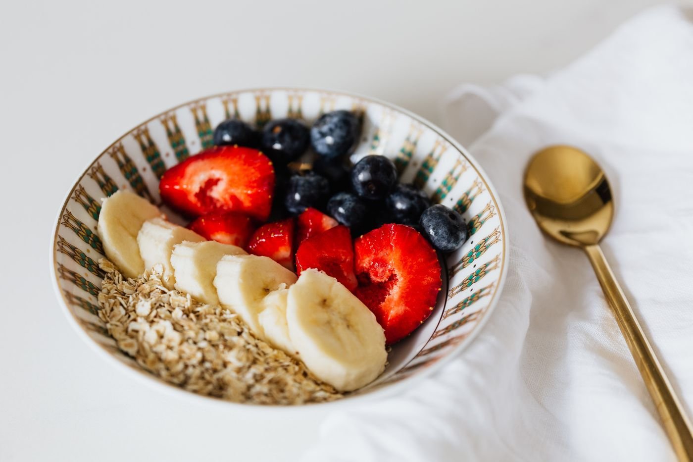 Bowl of muesli with banana slices, strawberries and blueberries, gold spoon
