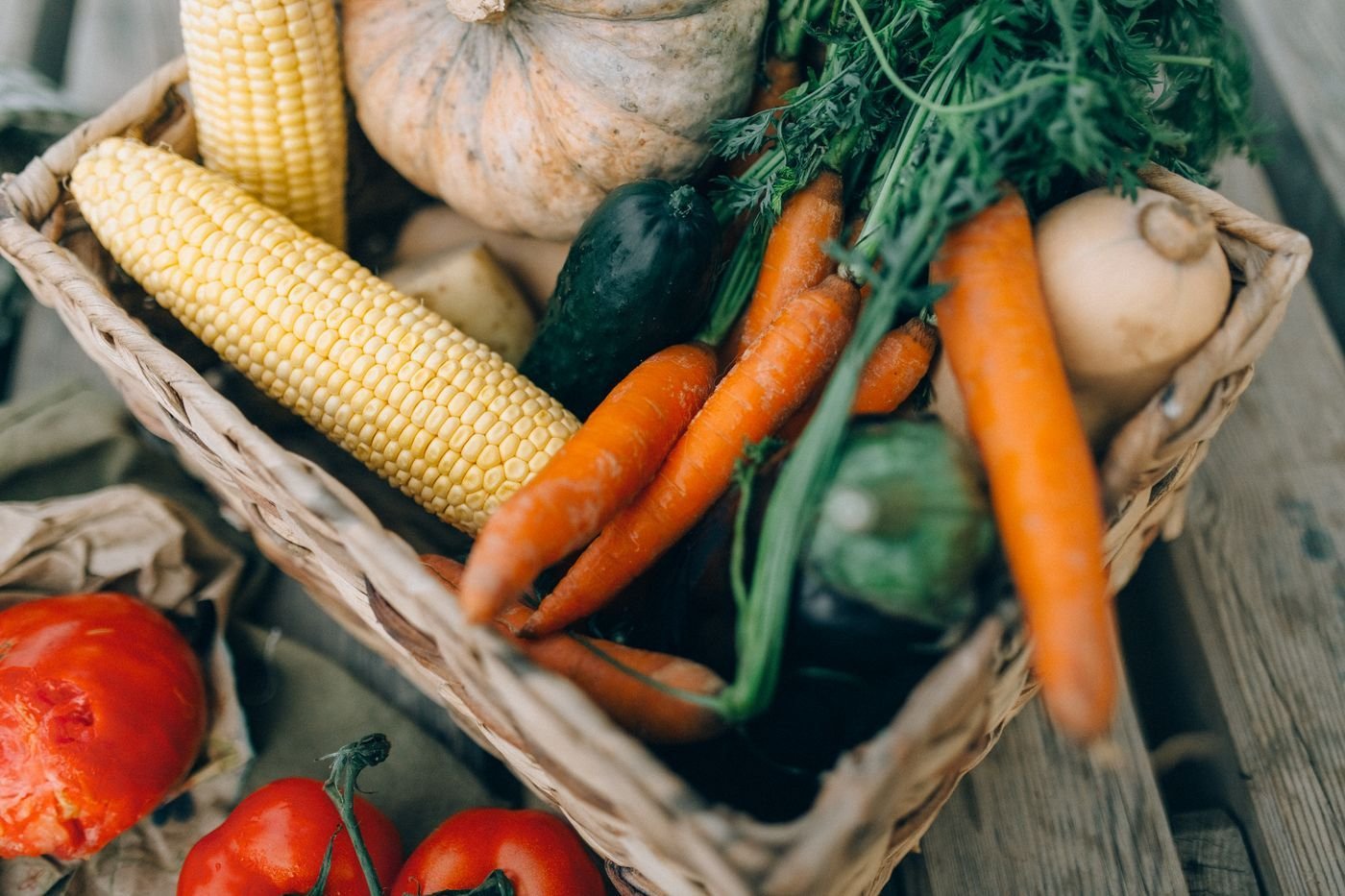 Basket of carrots, corn, squash and greens on a wooden table