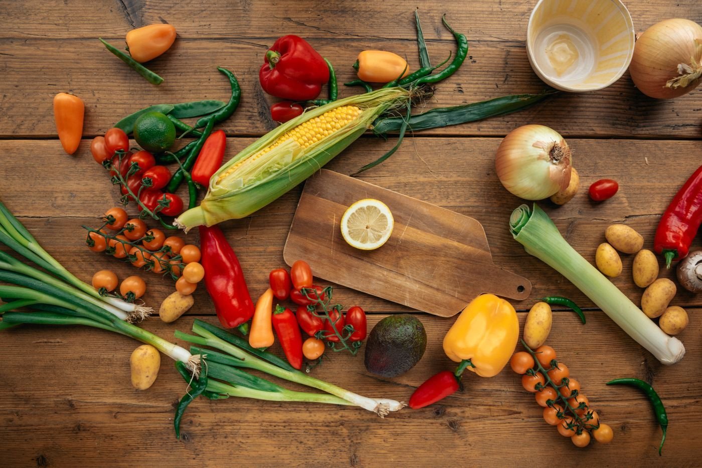 Flat lay of corn, peppers, tomatoes, leeks and lemon on rustic wood