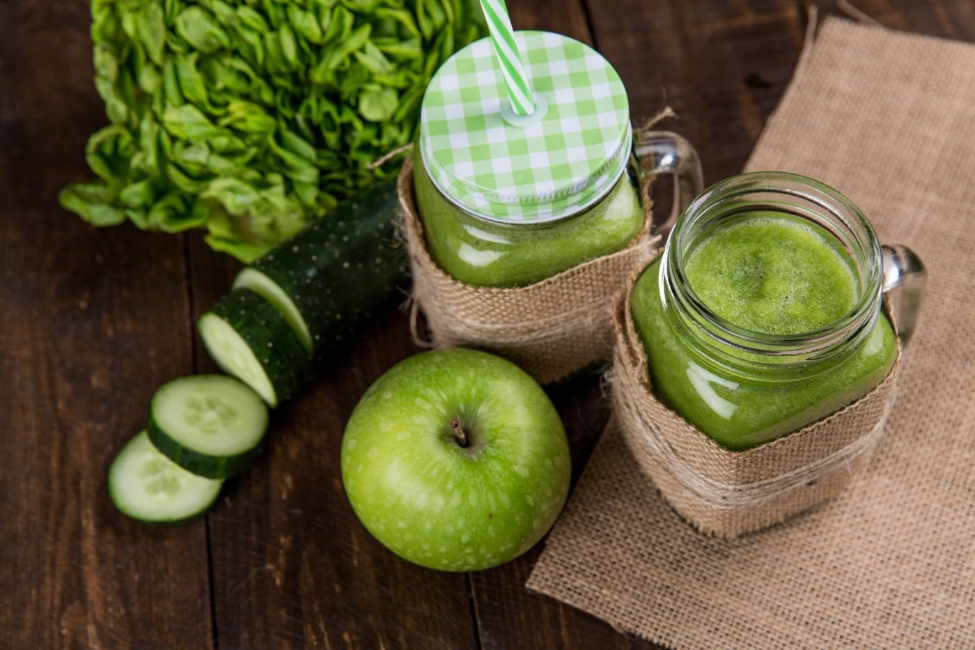 Two burlap-wrapped mason jars of cucumber apple green juice